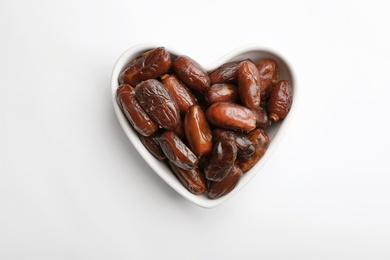 Photo of Heart shaped bowl with sweet dried date fruits isolated on white, top view