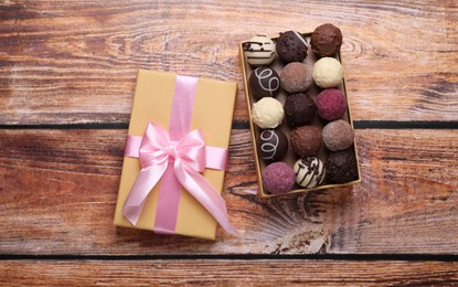 Photo of Open box with delicious chocolate candies on wooden table, top view