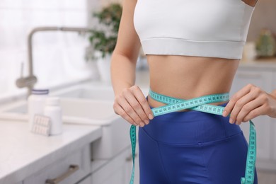 Photo of Slim woman measuring waist with tape in kitchen, space for text. Weight loss