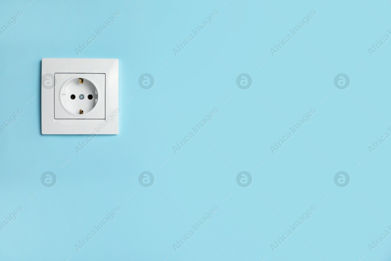 Photo of Power socket on light blue wall, space for text. Electrical supply