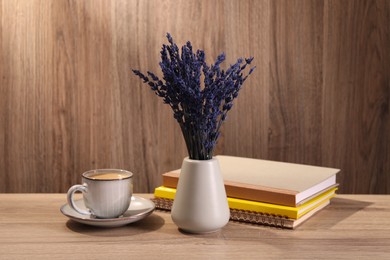 Photo of Bouquet of beautiful preserved lavender flowers, notebooks and cup of coffee on wooden table indoors