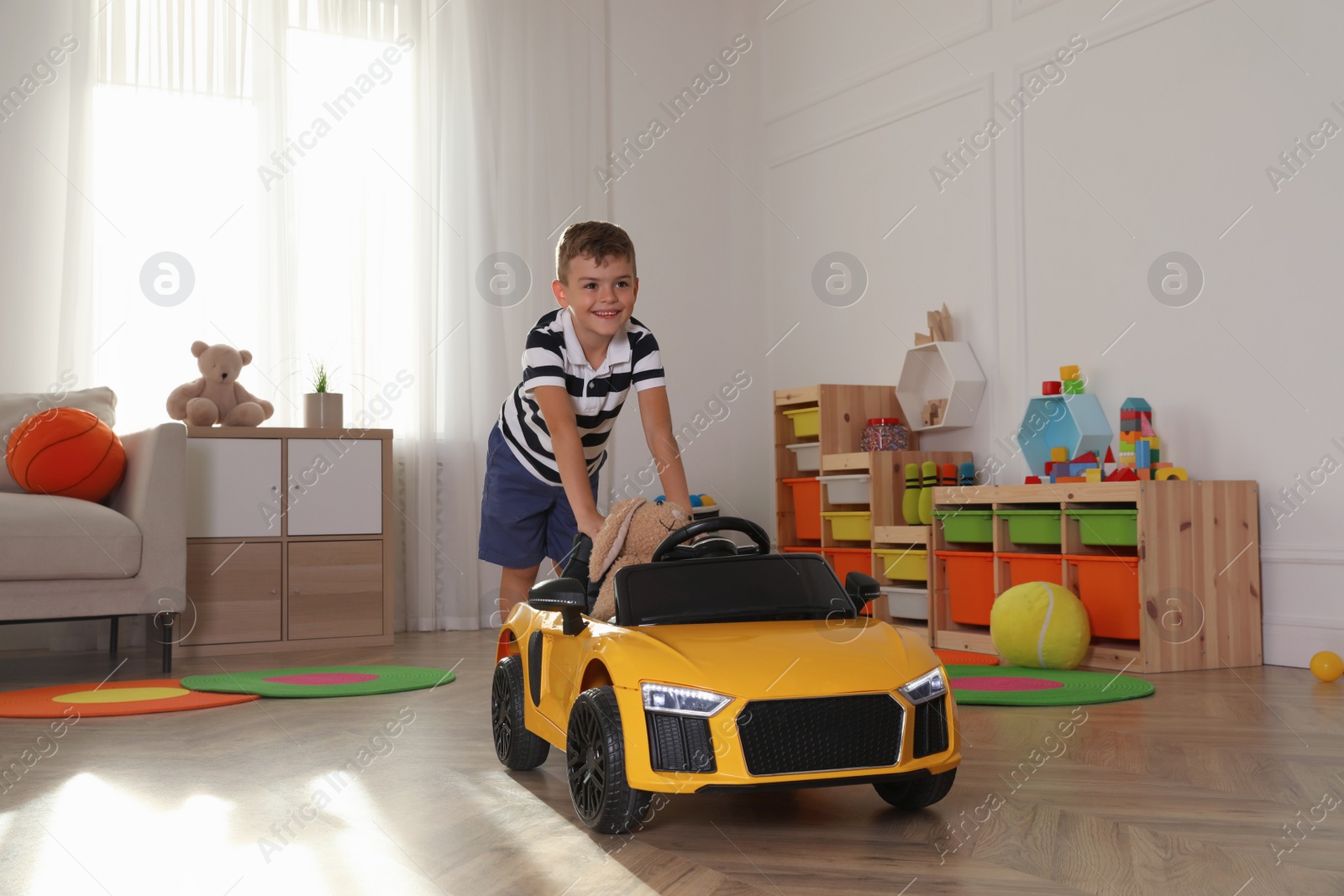 Photo of Cute little boy playing with big toy car and stuffed bunny at home