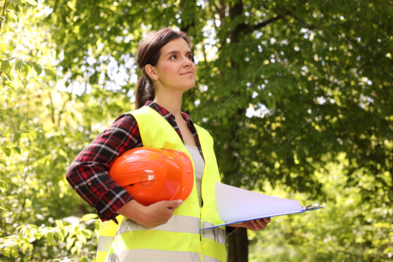 Photo of Forester with hard hat and clipboard examining plants in forest