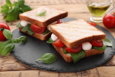 Photo of Delicious Caprese sandwiches with mozzarella, tomatoes, basil and pesto sauce on wooden table