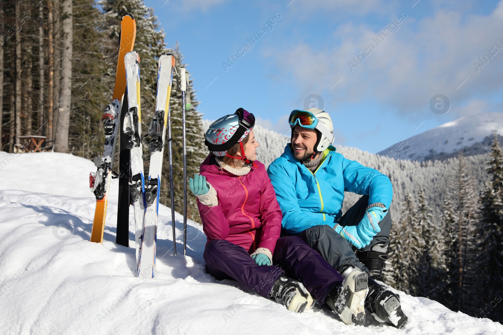 Photo of Happy couple with ski equipment sitting on snow in mountains. Winter vacation