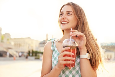 Photo of Young woman with refreshing drink on city street. Space for text