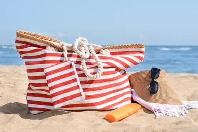 Photo of Stylish striped bag with beach accessories on sand near sea