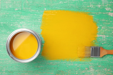 Can of yellow paint and brush on green wooden background, flat lay. Space for text