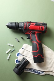 Photo of Electric screwdriver, gloves and accessories on pale green background, flat lay