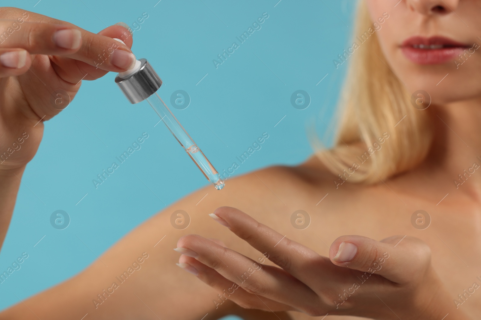 Photo of Woman applying cosmetic serum onto her hand on light blue background, closeup