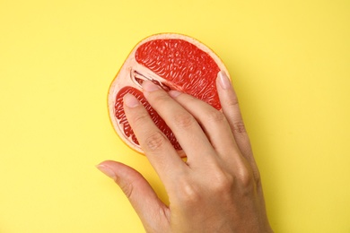Photo of Young woman touching half of grapefruit on yellow background, top view. Sex concept