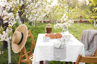 Photo of Stylish table setting with beautiful spring flowers, tea and croissants in garden