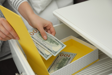 Photo of Woman hiding dollar banknotes in box at home, closeup. Money savings