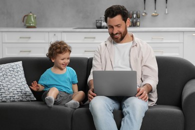 Photo of Cute little boy and his father with laptop at home