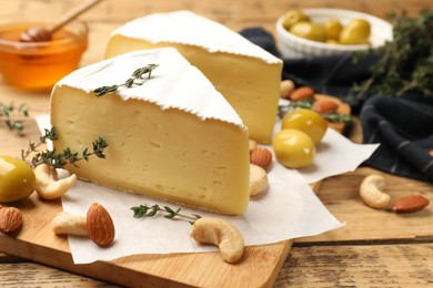Photo of Tasty Camembert cheese with thyme, olives and nuts on wooden table, closeup