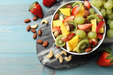 Photo of Tasty fruit salad in bowl and ingredients on light blue wooden table, flat lay. Space for text