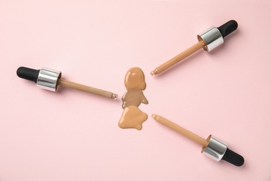 Photo of Samples of different foundation shades and droppers on pink background, top view