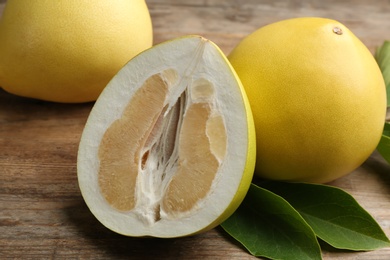 Photo of Fresh cut and whole pomelo fruits on wooden table, closeup