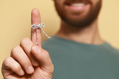 Photo of Man showing index finger with tied bow as reminder against beige background, focus on hand