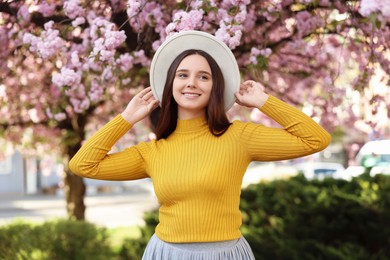Photo of Beautiful woman in hat near blossoming tree on spring day
