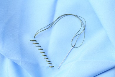 Photo of Sewing needle with thread and stitches on light blue cloth, top view