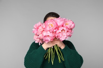 Photo of Young woman covering her face with bouquet of peonies on light grey background