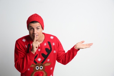 Photo of Man in Christmas sweater and hat showing silence gesture on white background