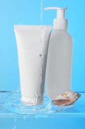 Photo of Pouring water on face cleansing products, petri dish and seashell against light blue background