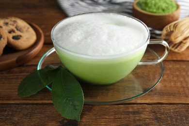 Photo of Cup of fresh matcha latte and green leaves on wooden table, closeup