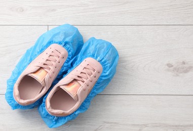 Photo of Women`s sneakers in blue shoe covers on light wooden floor, top view. Space for text