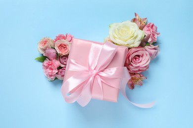 Photo of Gift box and beautiful flowers on light blue background, flat lay