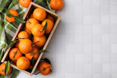 Photo of Wooden crate with fresh ripe tangerines and leaves on white tiled table, flat lay. Space for text