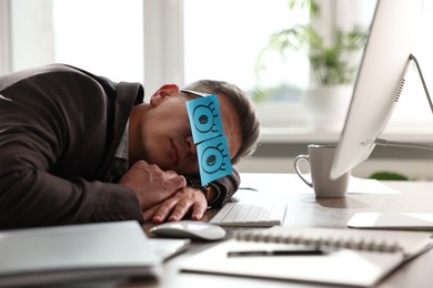 Photo of Man with fake eyes painted on sticky notes snoozing at workplace in office
