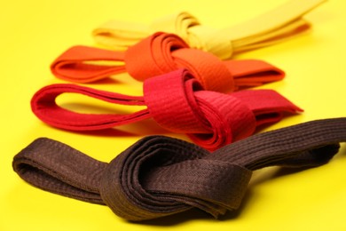 Photo of Colorful karate belts on yellow background, closeup