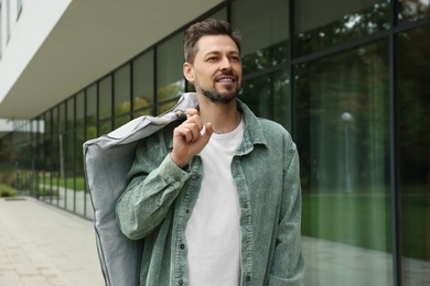 Photo of Attractive happy man holding garment cover with clothes outdoors. Dry cleaning service