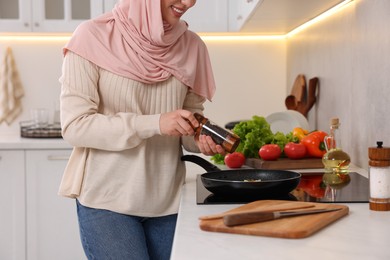 Photo of Muslim woman cooking delicious dish with vegetables on cooktop in kitchen, closeup