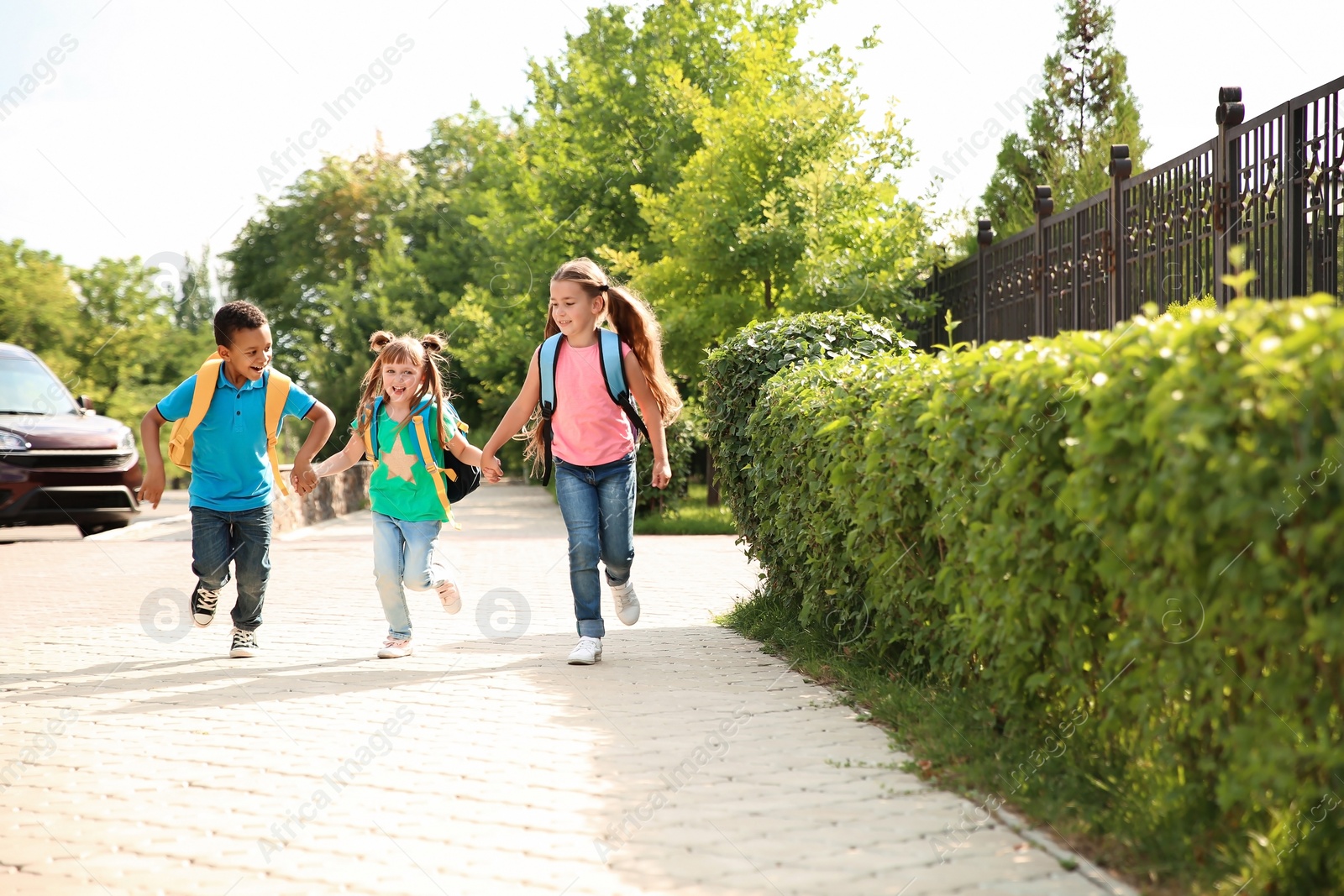 Photo of Cute little children with backpacks running outdoors. Elementary school