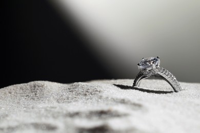 Photo of Luxury jewelry. Stylish presentation of ring in sand against dark background, closeup. Space for text