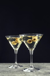 Photo of Martini cocktails with olives on grey table against dark background, space for text