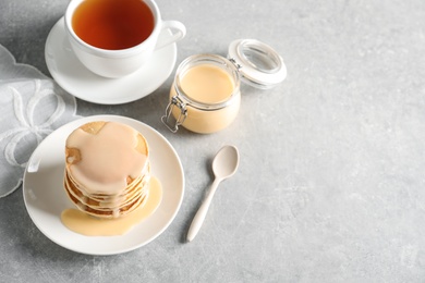 Photo of Composition with pancakes and condensed milk on grey background, space for text. Dairy product
