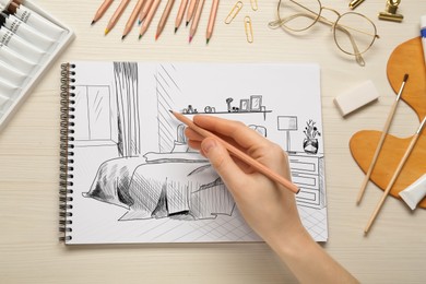 Image of Woman sketching bedroom interior in notebook with pencil at wooden table, top view