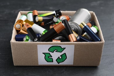 Image of Used batteries in cardboard box with recycling symbol on black table, closeup