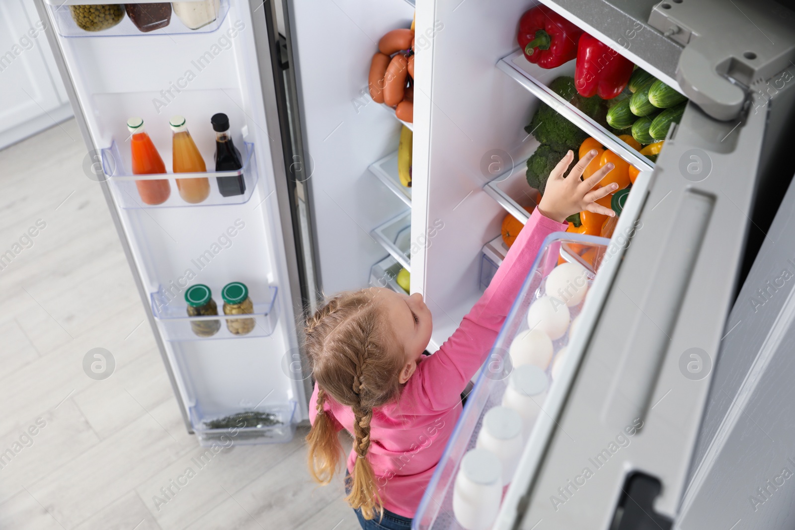 Photo of Little girl near open refrigerator indoors, above view