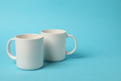 Photo of Two white ceramic mugs on light blue background, space for text