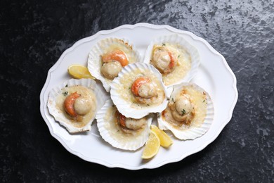 Photo of Fried scallops in shells and lemon on black textured table, top view