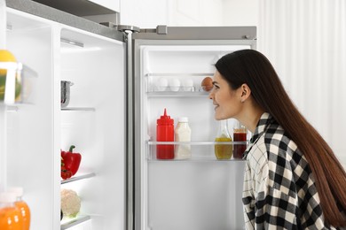 Photo of Young woman near modern refrigerator in kitchen
