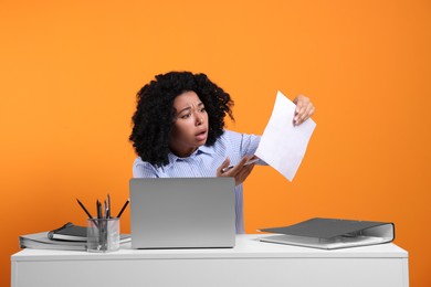 Photo of Stressful deadline. Emotional woman checking document at white desk against orange background