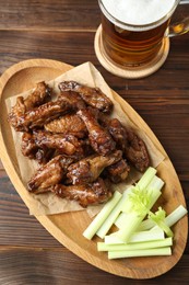 Photo of Delicious chicken wings served with cut celery stalks and beer on wooden table, flat lay