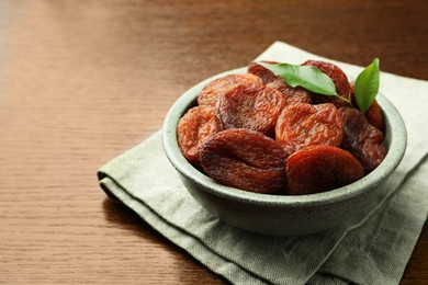Photo of Bowl of tasty apricots with leaves on wooden table, space for text. Dried fruits