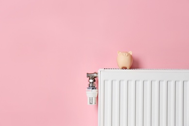 Photo of Heating radiator with piggy bank on color background. Space for text
